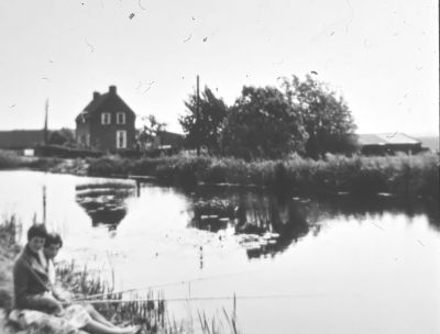 Gezicht op de woning van J. Griffioen, met schuur van W. Bon
De molen is reeds afgebroken. Op de voorgrond Tini en Ada van de Broek. 
J. Griffioen geboren 09-01-1907, overleden 27-09-1989.
echtgenote: G.E. Griffioen geboren 14-09-1907, overleden 17-11-1979.
Beiden begraven te Driemond.
