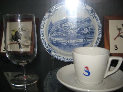 P. Sluis, fabriek pluimvee-, vee- en vogelvoeder 
Nogmaals de kop en schotel en een wijnglas, beide met het logo, en verder een asbak met een overzicht van het Sluisfabriekscomplex in blauw-wit. Hier ligt Sluis niet specifiek in Geinbrug, maar in Weesperkarspel!
Keywords: Geinbrug;Driemond;Sluis,pluimvee;vee;vogel;voeder;reclame;merchandise